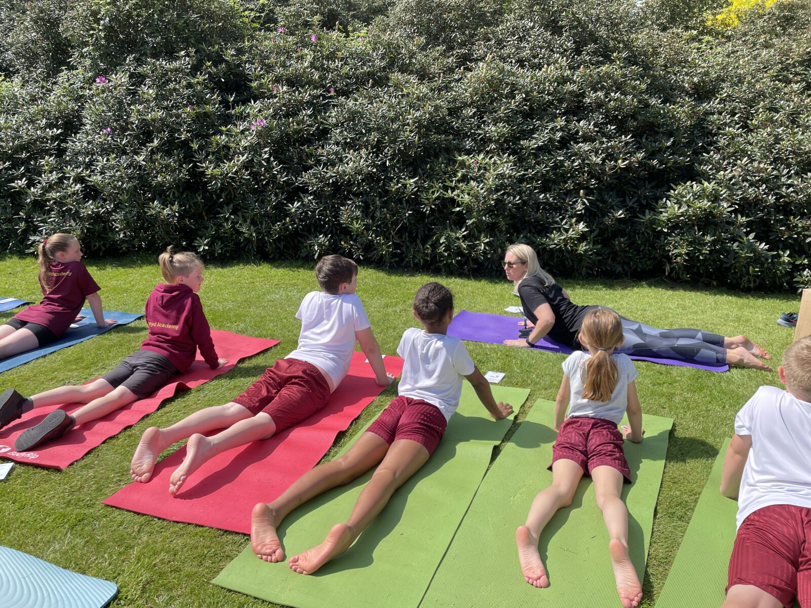 Teacher and children practising yoga on school lawn