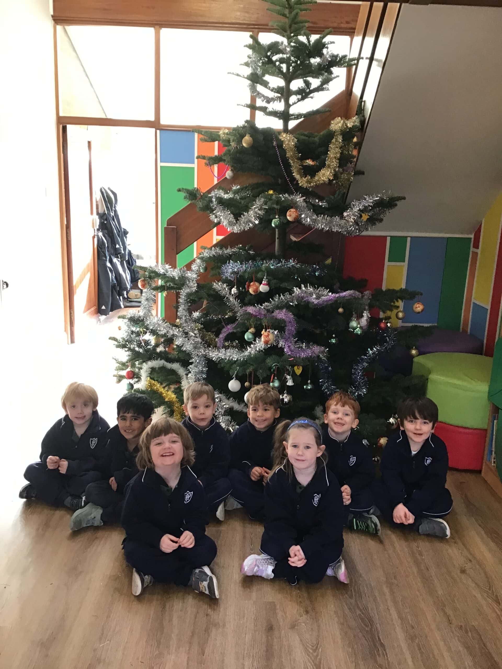 Young children sitting around a Christmas tree
