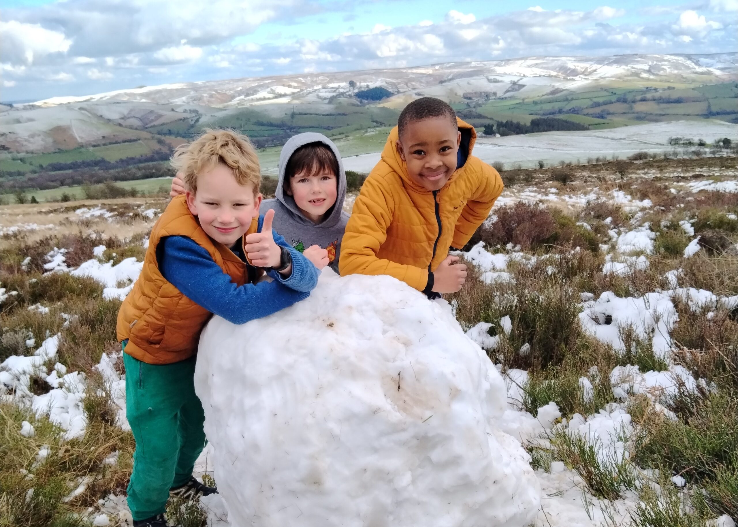 Three children building a snowman in the Shropshire hills